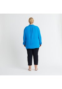 Blaue Bluse mit langen Ärmeln und einem Halstie, kombiniert mit eng anliegenden schwarzen, cropped Hosen. Glatter Stoff mit entspanntem Schnitt.