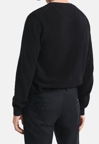 Pull noir avec un design en maille texturée, col rond, et manches longues ; assorti à un pantalon foncé avec poches arrière et détails à boutons.