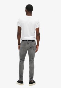 Jeans gris de corte ajustado con bolsillos traseros, combinados con una camiseta blanca y un cinturón negro. El atuendo incluye zapatillas negras con suelas blancas.