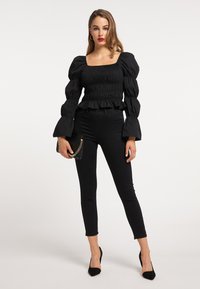 Sort puffærmet top med samlet tekstur, firkantet udskæring og flæsekant, parret med sorte tætsiddende jeans og sorte spidse hæle.
