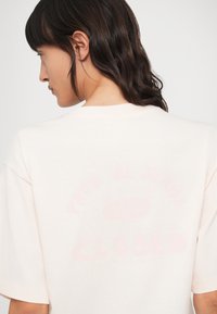 Camiseta oversize de color rosa claro hecha de tela suave, con texto descolorido 'CLOSED' y 'PROD. JEANS 1976' impreso en la espalda.