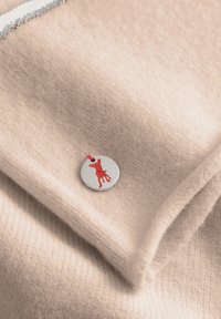 Lichtroze kasjmier stof met een gladde textuur, voorzien van een ronde zilveren tag met een rode hondensilhouet eraan bevestigd.