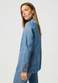 Vaaleansininen farkkutakki pitkillä hihoilla, nappikoristeilla hihansuissa ja rento istuvuus. Ominaisuuksiin kuuluu klassinen ompelu ja siisti muotoilu.