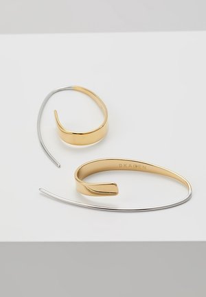 Kaksi minimalistista metallikorvakorua, joissa on kullanväriset kaarevat osat ja ohuet hopeaiset koukkukiinnikkeet valkoisella pinnalla.