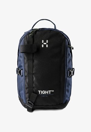 Sac à dos compact bleu marine et noir avec poignée supérieure, sangles frontales, boucles latérales, et "TIGHT™ X SMALL" imprimé sur le panneau avant.