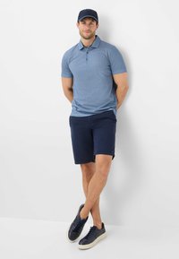Polo a maniche corte di colore blu con un leggero motivo, abbinato a pantaloni corti blu scuro e sneakers blu scuro, completato da un cappellino coordinato.