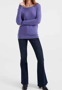 Maglione viola a coste con maniche lunghe e scollo a barca, abbinato a jeans in denim scuro a gamba larga. Tessuto liscio con dettagli di motivo sottili.