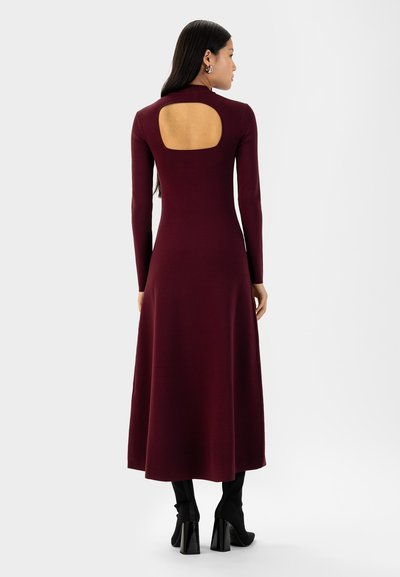 Vestito borgogna a maniche lunghe con schiena scoperta, lunghezza midi morbida, realizzato in tessuto morbido. Abbinato a stivaletti neri con tacco.