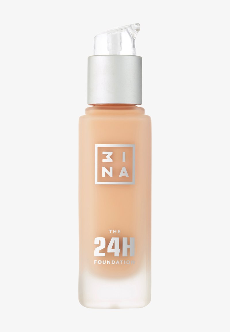 Base en un frasco de cristal transparente con dispensador de bomba. Presenta una tapa plateada y un branding impreso en blanco y plateado en el frente.