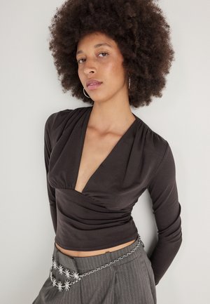Haut noir à manches longues avec un décolleté en V profond et un tissu froncé au niveau de la poitrin. Associé à un pantalon gris à rayures fines et une ceinture en chaîne argentée.