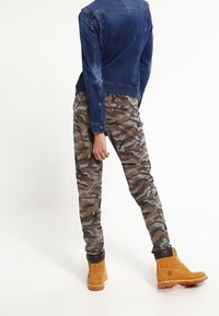 Jeansjacka med nitar, kombinerad med byxor i camouflage-mönster och tanfärgade ankelstövlar. Synliga texturer och mönster framhävs.