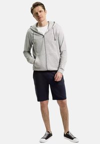 Szara bluza z zamkiem na całej długości, z regulowanym sznurkiem, w połączeniu z ciemnymi szortami i czarnymi sneakersami. Charakteryzuje się luźnym krojem i prostym, eleganckim designem.