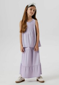 Tenue deux pièces lilas comprenant un top sans manches en tissu texturé et une jupe maxi à volants. Associée à des baskets blanches.