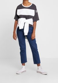 Camiseta gris y blanca a rayas con un corte relajado, combinada con unos vaqueros cortos azules y zapatillas altas blancas. Sudadera blanca atada a la cintura.