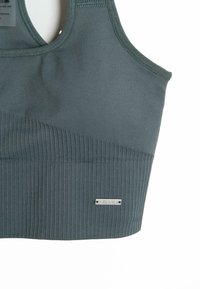 Sujetador deportivo en tela azul oscuro, con una banda elástica acanalada, parte superior suave y un pequeño logo metálico. Textura suave, diseño ergonómico.