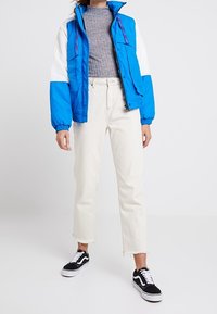 Blaue und weiße, farbige Block-pufferjacke mit hohem Kragen, kombiniert mit hellbeigen, cropped Jeans und schwarzen Sneakers mit weißen Akzenten.