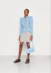 Lyseblå denim skjorte med puff ermer, knappfront og belte. Kombinert med et rutete miniskjørt og brune sandaler, bærende en lyseblå veske.