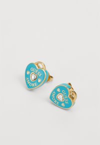 Boucles d'oreilles en forme de cœur en ton doré, ornées d'émail turquoise, du texte "GUESS AMORE", d'un cristal central en forme de cœur et de petits accents transparents.