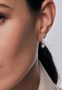 Złote kolczyki z trzema przezroczystymi, okrągłymi kryształami ułożonymi w opadającym wzorze, zaprezentowane na neutralnym tle.