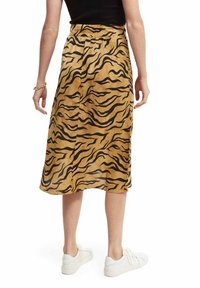 Tan midi rok met een zwart tijgerprintpatroon, gemaakt van gestructureerde stof, met een getailleerde taille en een zijsplit, gecombineerd met witte sneakers.