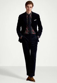 Marineblå fløyelsdress med en tettsittende design, fremhevet av en rutete skjorte. Teksturert stoff, skreddersydd passform og brune semskede sko fullfører antrekket.