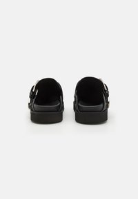 Les sandales noires présentent une tige en cuir lisse, un large talon et une sangle à boucle ajustable. L'intérieur est rembourré pour le confort.