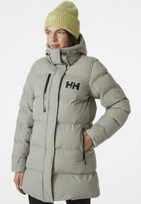 Svetlosivá prešívaná bunda s vertikálnou prešívanou textúrou, vysokým golierom, predným zipsom a čiernym logom. Doplnok tvorí svetlo zelená rebrovaná čiapka.