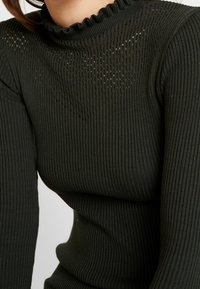 Mörkgrön, ribbads turtleneck-tröja med ett texturerat, öppet stickat mönster under halsringningen och en volangkrage.