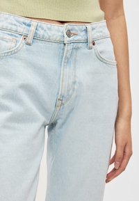 Ανοιχτό μπλε τζιν παντελόνι με ψηλή μέση, σχεδιασμό με πέντε τσέπες και κούμπωμα με κουμπί. Διαθέτει διακριτική ξεθώριαση και αντίθετα γαζιά.