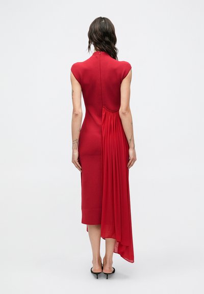 Czerwona sukienka z krótkimi rękawkami typu cap, dopasowaną górą i zwiewnym tyłem wykonana z miękkiego materiału z teksturowanym akcentem.