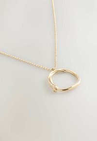 Gouden ketting met een ronde hanger met een gladde afwerking, versierd met kleine heldere stenen aan één kant, bevestigd aan een delicate ketting.