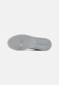 Podeszwa sneakersów Nike w jasnoszarym kolorze, z okrągłymi i bieżnikowymi wzorami, z wyraźnym logo Nike oraz teksturowanym wykończeniem z gumy.