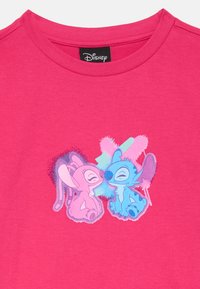 Tricou din bumbac roz fluorescent, prezentând o grafică cu două personaje din desene animate, unul roz și unul albastru, cu expresii jucăușe pe un fundal colorat.