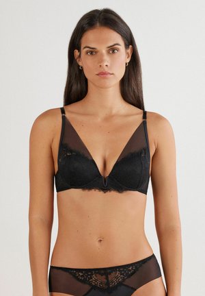 Soutien-gorge noir avec des accents en dentelle, des panneaux en maille transparente et un décolleté plongeant. Les bretelles réglables et les bords festonnés soulignent le design.