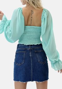 Top corto smock verde menta con maniche a palloncino abbinato a una mini gonna di jeans strappata con orlo distrutto e due tasche posteriori.