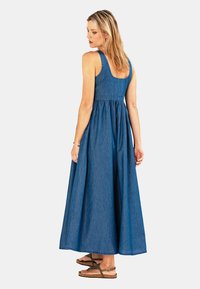 Denim maxi-jurk met een getailleerde bustier, brede banden en een vloeiende rok. Kleur: middelblauw met een gladde textuur. Sandalen maken de outfit compleet.