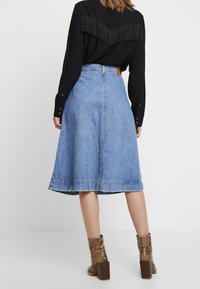 Jeans-midi kjol i ljusblått med en utsvängd form och fransad fåll. Kombination med en svart skjorta som har en fransad detalj på ryggen och klackskor med ormskinnsmönster.