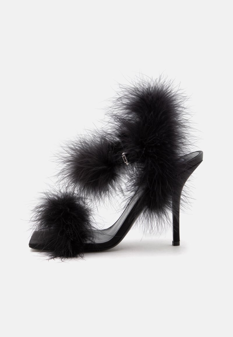 Sandale noire à talon haut avec des accents de plumes duveteuses sur l’orteil, la bride de cheville et la bride de talon sur fond blanc.
