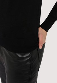 Svart stickad tröja med långa ärmar, med en ribbad nederkant. Kombinerad med eleganta svarta läderbyxor som visar en slät textur och passform.