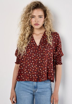 Maroon floral blouse with short elastic sleeves, v-neckline, and button closure. Pattern features small red and cream flowers on a textured fabric.