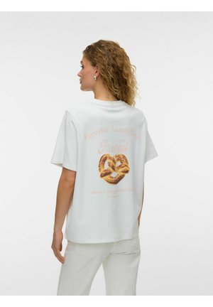 Moteris su garbanotais plaukais dėvi baltą marškinėlį su pretzelio grafika ir tekstu apie mėgstamus pietų kąsnelius, matoma iš nugaros.