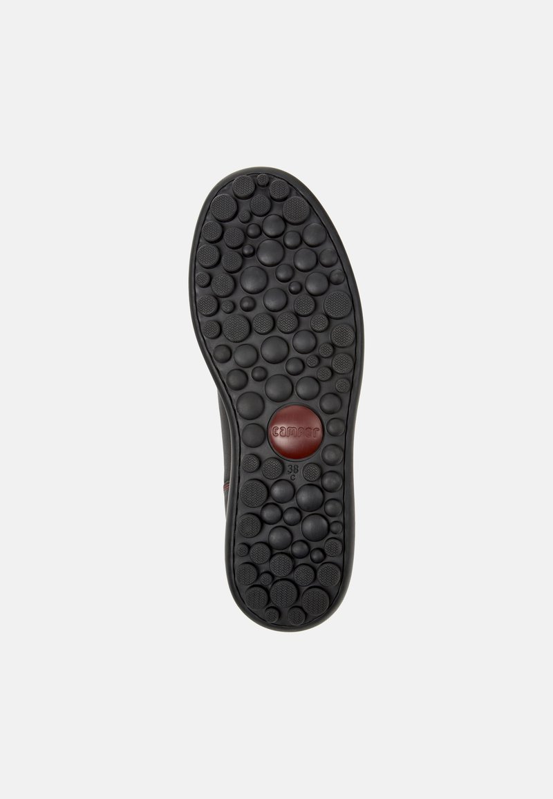 Suela de goma negra con una superficie texturizada y protuberancias redondas, acentuada por un logo circular rojo y el número de talla 38.