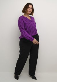 Blusa a maniche lunghe a righe viola con scollatura con bottoni, abbinata a pantaloni black a gamba larga e tacchi neri a punta.