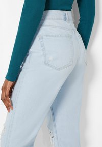 Vaaleansiniset korkeavyötäröiset farkut, joissa on rento malli, kahdella takataskulla ja kulutusta polvien lähellä. Pehmeä farkkukangas.