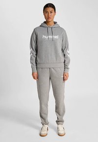 Grå hoodie- och byxset av mjukt tyg. Hoodien har dragsko och logotyp; byxorna har elastiska muddar och sidofickor.