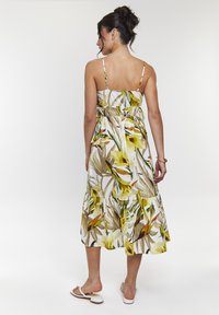 Vestido midi floral de tejido ligero que presenta patrones botánicos en amarillo y verde, tirantes finos ajustables y un dobladillo en capas.
