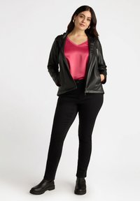 Schwarze Kunstlederjacke mit Kapuze, kombiniert mit einem lebendigen pinken Satinoberteil und schwarzen engen Hosen, ergänzt durch schwarze Ankle Boots.