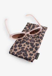 Világos rózsaszín áttetsző macskaszem napszemüveg egy összehajtott barna leopárdmintás puha textil zsákon nyugszik, amelyen egy kis fekete címke található.