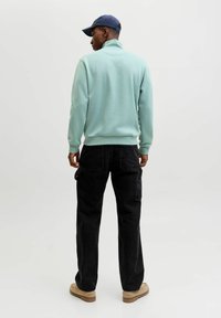 Felpa azzurro chiaro con colletto alto, pantaloni cargo neri e scarpe beige. La vista posteriore mostra la vestibilità comoda e la texture della felpa.