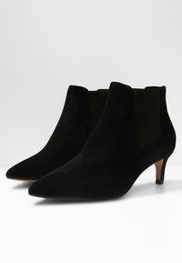 Svarta mocka ankstövlar med spetsiga tår, elastiska sidor och låg klack. Slät textur med en minimalistisk design.